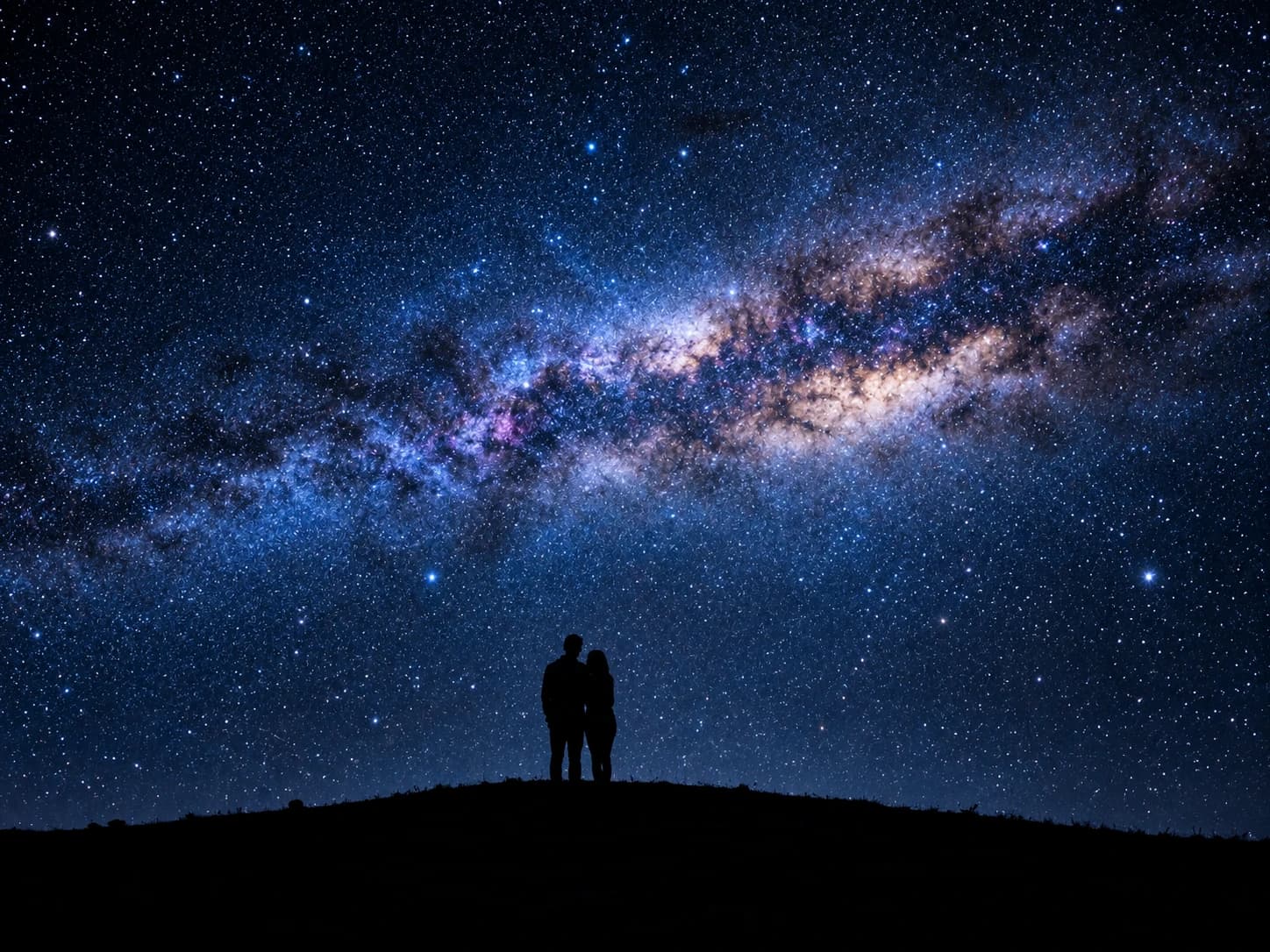 A couple standing on a hill under the Milky Way