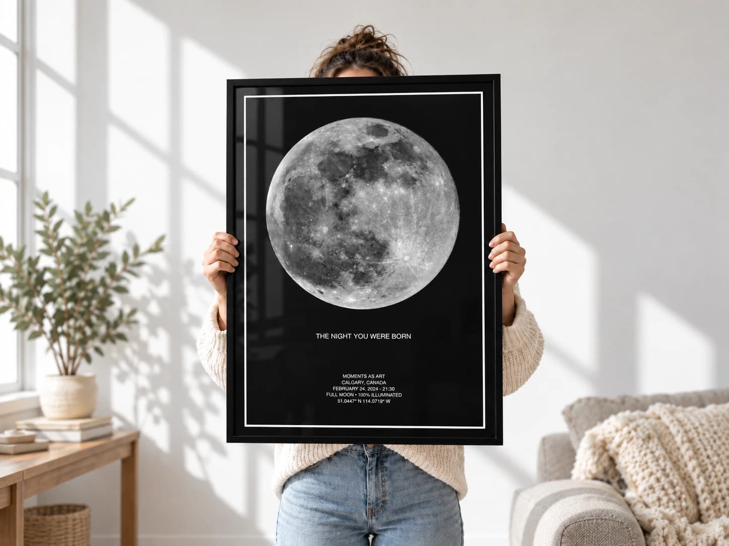 Someone holding up a framed black moon print titled The Night You Were Born in a sunlit living room
